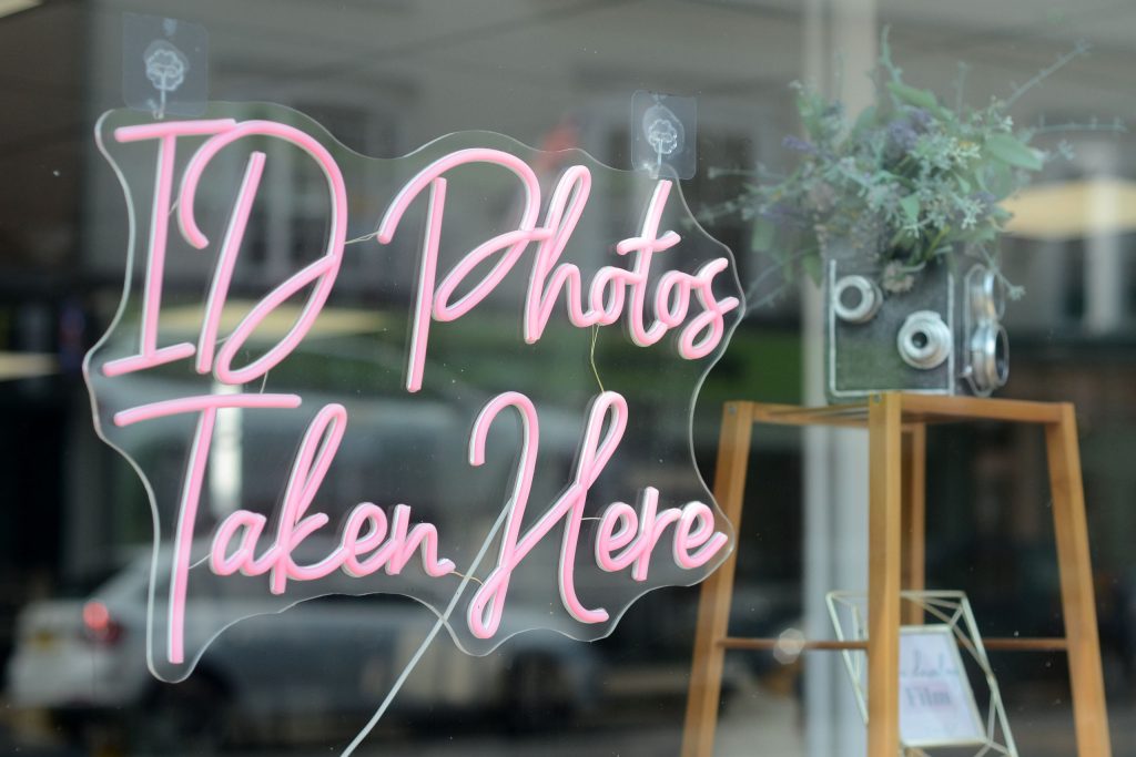 Neon sign saying "ID Photos Taken Here" in Boho Photo shop window