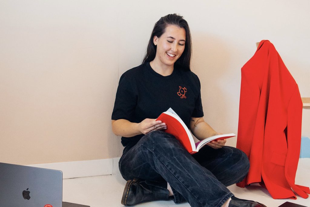Danielle Goody of Goody Creative setting crosslegged on the floor reading a large red book