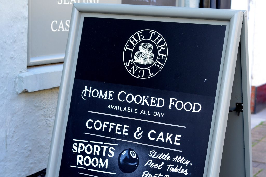 The Three Tuns A-frame sign in Honiton High Street advertising home cooked food, coffee and cake and a sports room