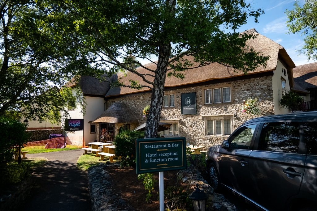 Side view of the Heathfield Inn an old thatched building with picnic tables under trees