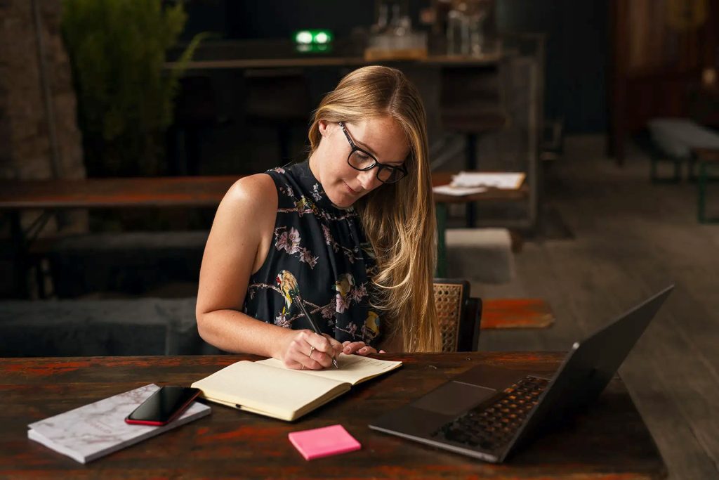 Amy Sugrue On Point VA sitting at wooden table with phone and laptop writing in a notepad